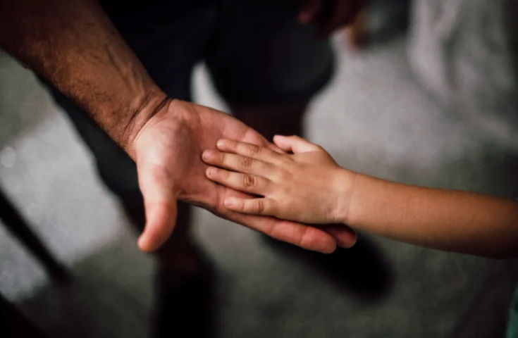 A dad holds his child's hand.