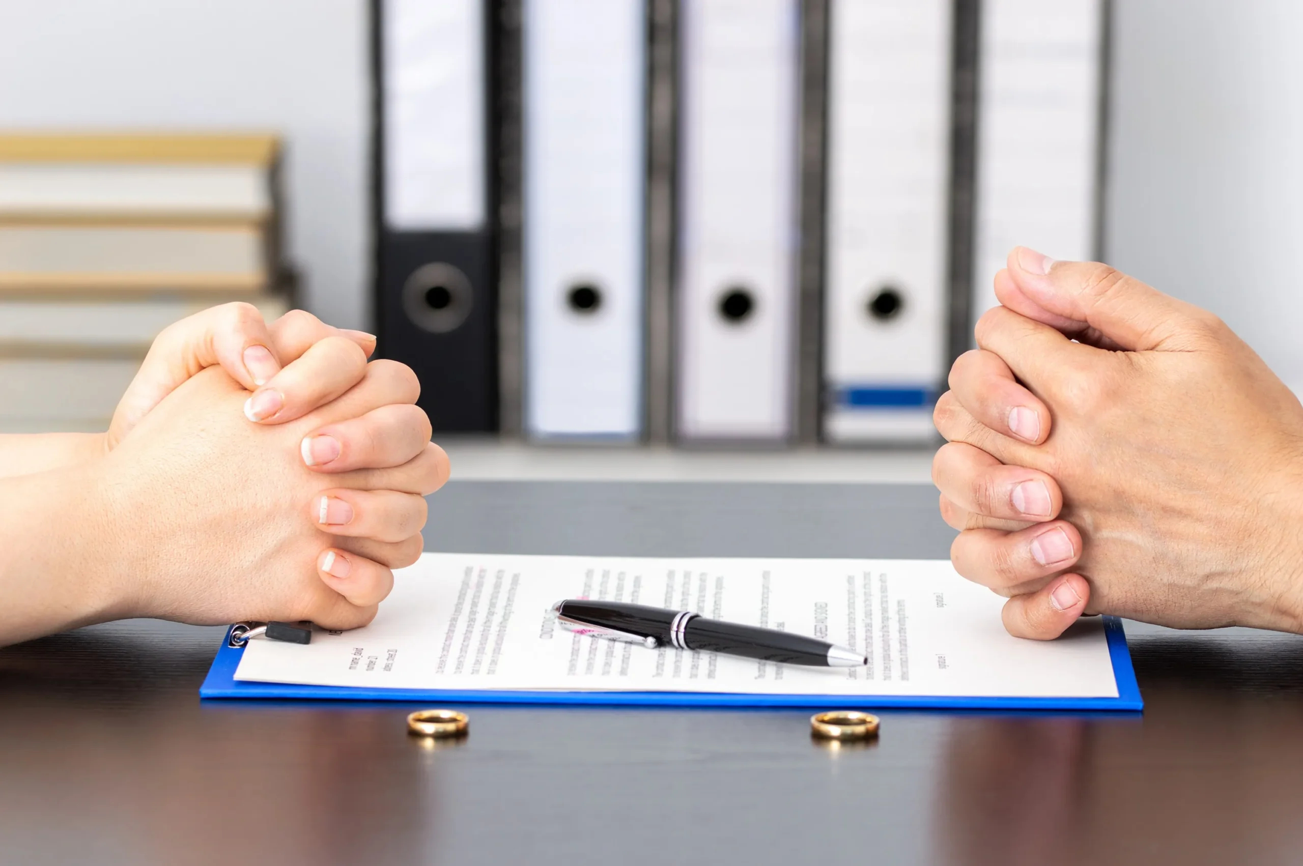 A couple with hands crossed sitting over paperwork.