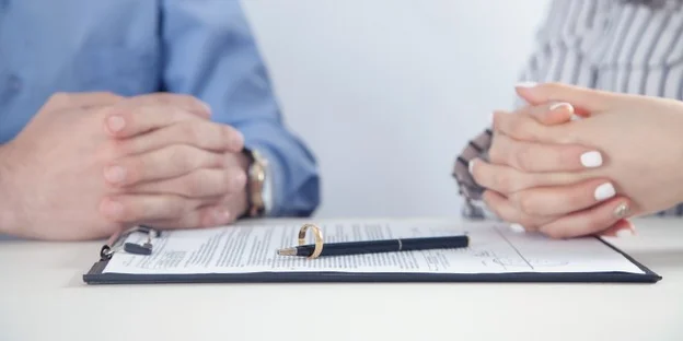 Two people sitting across from each other with a document and pen between them.