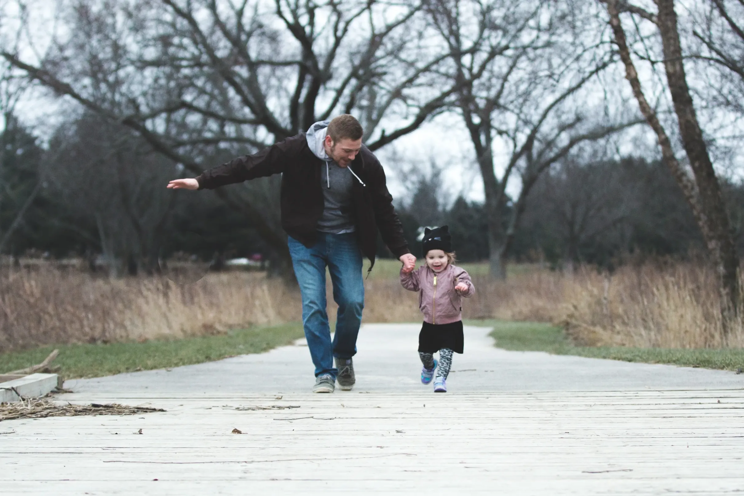 A father holding his daughter's hand walking outside.