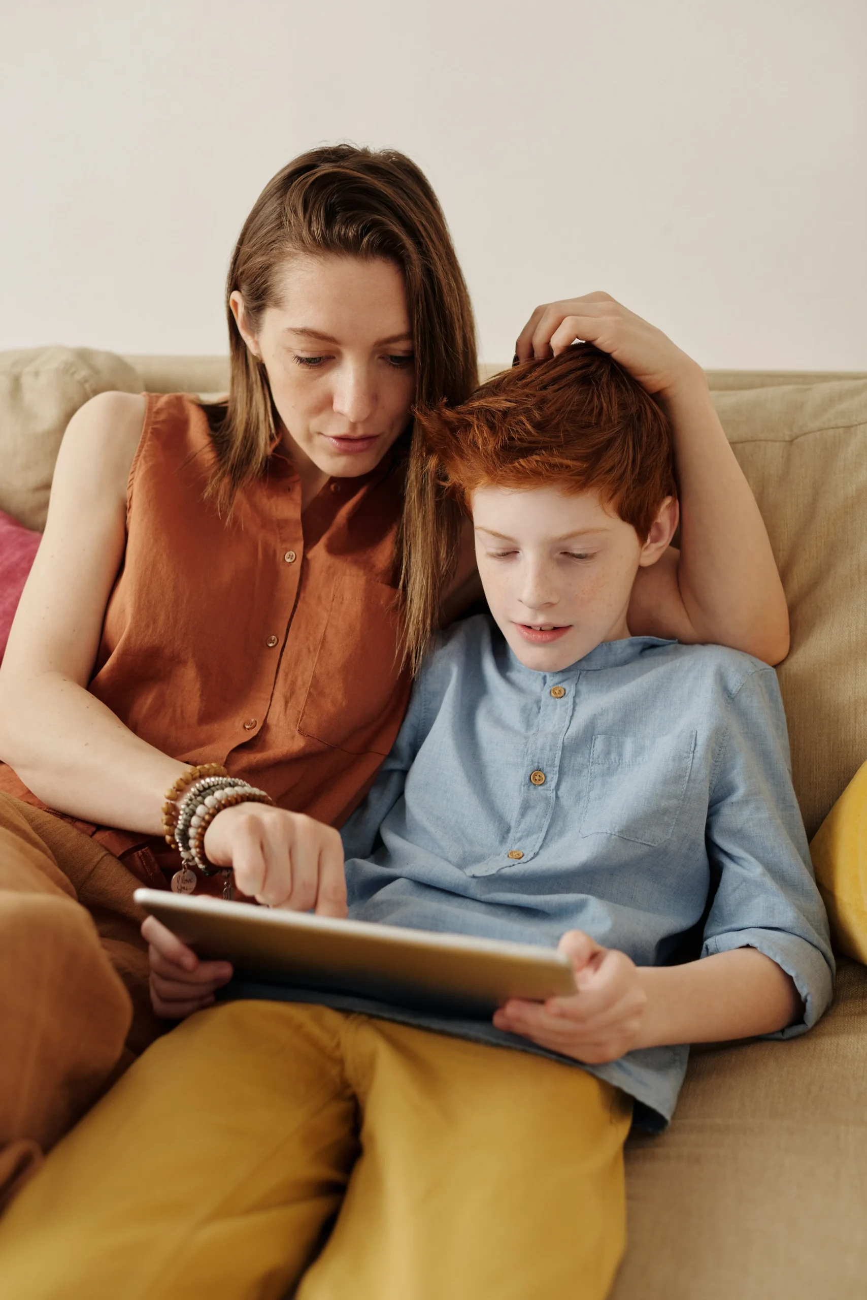 A mom and teenager sitting on a couch, interacting with a tablet computer.