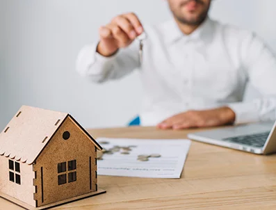 Person sitting at a table with documents, coins and a house model.